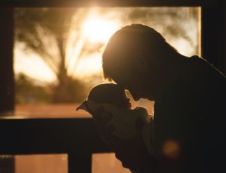 National Baby Day 2022 - Silhouette of man holding a baby, sunset background - Blog Thumbnail