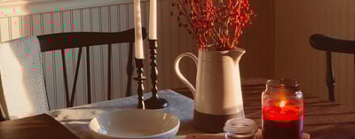 table with white bowl, red candle, jug vase with red berry branches and candlesticks