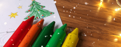 red, orange, green and yellow crayons on a colouring sheet with some christmas lights nearby